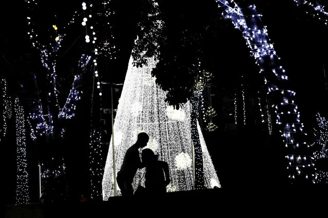 A couple rests near a Christmas tree located at the Supreme Court (TSJ) building on Bolivar Avenue in Caracas, Venezuela, Sunday, January 2, 2022. (Photo by Matias Delacroix/AP Photo)