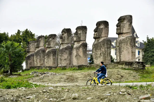 A man rides a bicycle past replicas of the Moai statues of Easter Island at a college built on the site of a former theme park in Chengdu in southwestern China's Sichuan province Tuesday, March 28, 2017. Chinese developers and institutions have drawn worldwide attention in recent years for building replicas of everything from the Eiffel Tower to the Sphinx. (Photo by Chinatopix via AP Photo)