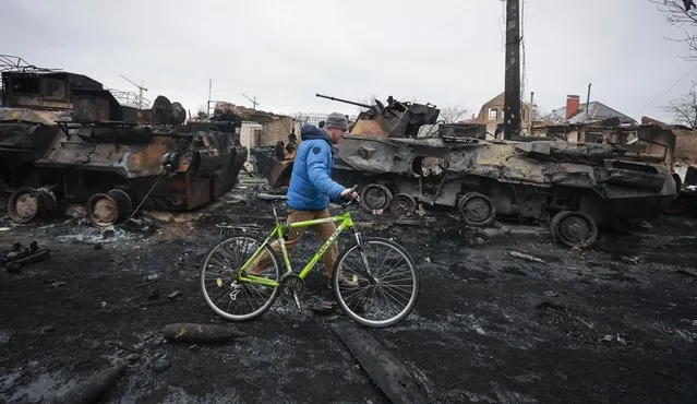 A man walks past the remains of Russian military vehicles in Bucha, close to the capital Kyiv, Ukraine, Tuesday, March 1, 2022. Russia on Tuesday stepped up shelling of Kharkiv, Ukraine's second-largest city, pounding civilian targets there. Casualties mounted and reports emerged that more than 70 Ukrainian soldiers were killed after Russian artillery recently hit a military base in Okhtyrka, a city between Kharkiv and Kyiv, the capital. (Photo by Serhii Nuzhnenko/AP Photo)