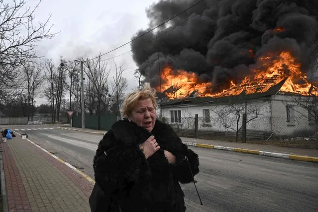 A woman reacts as she stands in front of a house burning after being shelled in the city of Irpin, outside Kyiv, on March 4, 2022. (Photo by Aris Messinis/AFP Photo)