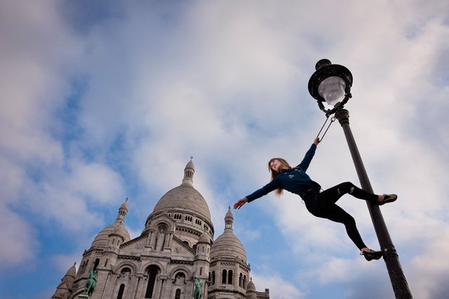 France's climber Capucine Viglione poses on a street lamp in front of the Sacre-Coeur Basilica (Sacred Heart) in Paris on May 22, 2024, ahead of the Paris 2024 Olympic and Paralympic games. The Basilica of the Sacre-Coeur (Sacred Heart) is located on the top of Montmartre hill in Paris. Pope Benedict XV elevated it to the rank of minor basilica in 1919. (Photo by Franck Fife/AFP Photo)