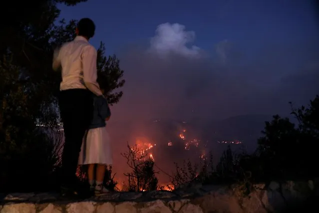 A man and his daughter watch as wildfire burns on the opposite mountain near Shoeva, on the outskirts of Jerusalem on August 15, 2021. (Photo by Ronen Zvulun/Reuters)
