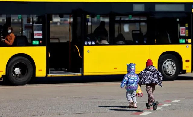 Two refugees kids from Ukraine, fleeing the Russian invasion of Ukraine, runs towards a bus at a newly built arrival centre on the tarmac of the former Tegel airport in Berlin, Germany, March 22, 2022. (Photo by Hannibal Hanschke/Reuters)