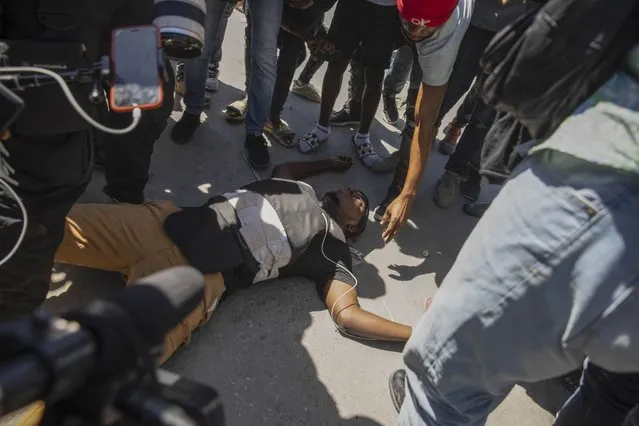 Haitian photojournalist Maxihen Lazzare lies dead on the ground, after he was shot while covering a protest by factory workers demanding higher salaries in Port-au-Prince, Haiti, Wednesday, February 23, 2022. Men wearing police uniforms drove by the protest and fired into the crowd of protesters where Lazzare was covering the demonstration. (Photo by Joseph Odelyn/AP Photo)