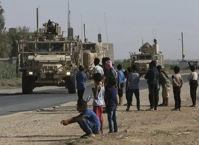 Syrian children and youths gather on a street as they look at a U.S. armored vehicle convoy pass on a road that links to Raqqa city, northeast Syria, Wednesday, July 26, 2017. (Photo by Hussein Malla/AP Photo)