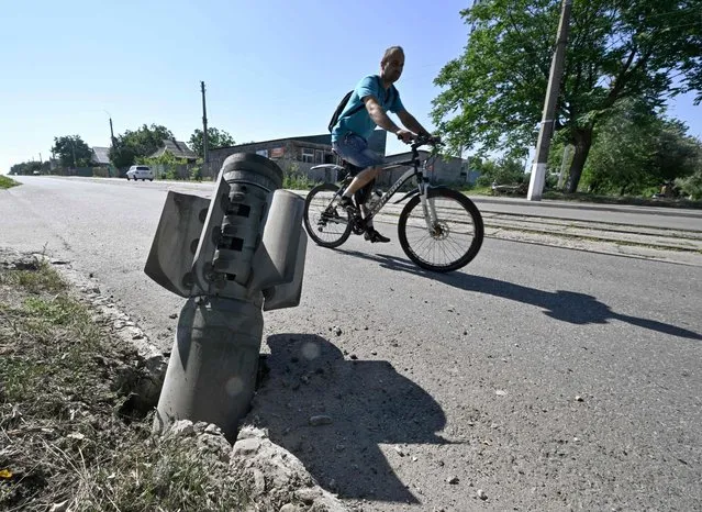 A cyclist rides past a tail section of a rocket embedded in a road in Kramatorsk on July 4, 2022, the day after a Russian rocket attack. (Photo by Genya Savilov/AFP Photo)