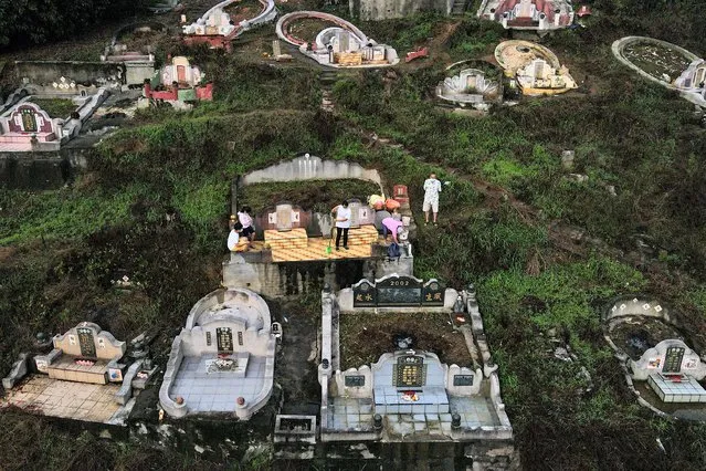 An aerial view shows a Chinese Malaysian family, with offerings of food and paper money, praying at the grave of an ancestor in a Chinese cemetery on the eve of the annual Qingming festival, also known as Tomb Sweeping Day, in Karak in Malaysia's Pahang state on April 4, 2022. (Photo by Mohd Rasfan/AFP Photo)