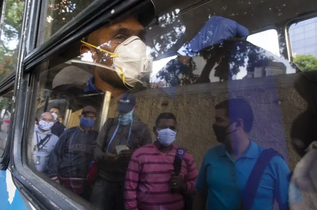 People wearing protective masks as a precaution against the spread of the new coronavirus are reflected on a bus window, in Caracas, Venezuela, Tuesday, March 17, 2020. President Nicolas Maduro ordered citizens to stay home, and to wear a mask when in public. The vast majority of people recover from the new virus. (Photo by Ariana Cubillos/AP Photo)
