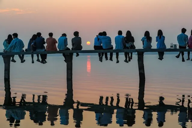 People sit on a footbridge as they watch the sunrise at the East Lake Park on September 30, 2022 in Wuhan, Hubei Province of China. (Photo by Chen Xuezi/VCG via Getty Images)