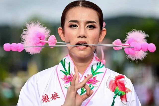 A devotee of the Jor Soo Gong Naka shrine with skewers pierced through her cheeks takes part in a procession during the annual Vegetarian Festival in Phuket on September 27, 2022. The festival, back after two years of hiatus because of the Covid-19 pandemic, features religious devotees who slash themselves with swords, pierce their cheeks with sharp objects and commit other painful acts to purify themselves, taking on the sins of the community. (Photo by Manan Vatsyayana/AFP Photo)