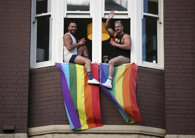 Two men watch a parade from a window as members of the gay community and their supporters celebrate the result of a postal survey calling for gay marriage right in Sydney, Australia, Wednesday, November 15, 2017. Australians supported gay marriage in a postal survey that ensures Parliament will consider legalizing same-s*x weddings this year. (Photo by Rick Rycroft/AP Photo)