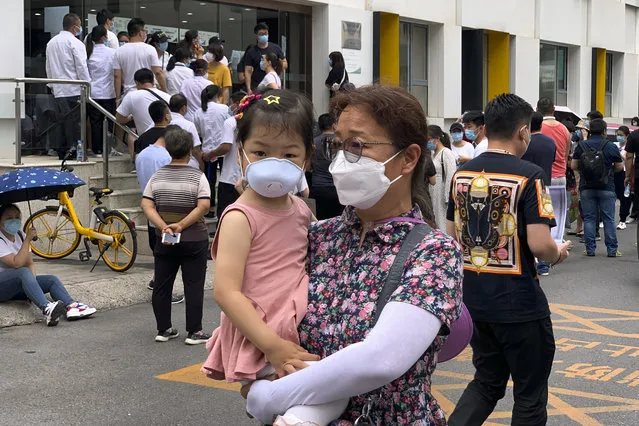 A woman and a child wearing protective face masks to help curb the spread of the new coronavirus walk by people lining up outside a health center to get the nucleic acid test in Beijing, Monday, June 15, 2020. China's capital was bracing Monday for a resurgence of the coronavirus after more than 100 new cases were reported in recent days in a city that hadn't seen a case of local transmission in more than a month. (Photo by Andy Wong/AP Photo)