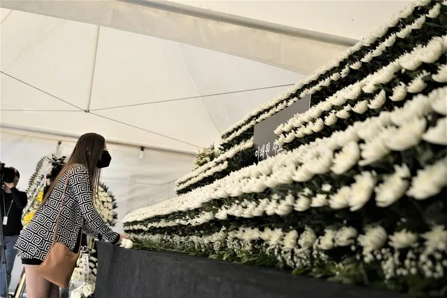 A mourner places flower to pay tribute for the victims of a deadly accident following Saturday night's Halloween festivities, at a joint memorial altar set near the scene in Seoul, South Korea, Monday, October 31, 2022. South Koreans mourned and searched for relatives lost in the “hell-like” chaos that killed more than 150 people, mostly young adults, when a huge Halloween party crowd surged into a narrow alley in a nightlife district in Seoul. (Photo by Lee Jin-man/AP Photo)