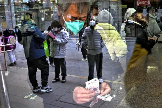 Visitors are reflected on a window pane as a man counts Chinese currency notes at a shop selling tea in Qianmen, a popular tourist spot in Beijing, Tuesday, January 3, 2023. As the virus continues to rip through China, global organizations and governments have called on the country start sharing data while others have criticized its current numbers as meaningless. (Photo by Andy Wong/AP Photo)