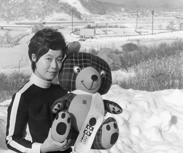 Pretty Press center employe, Kazuko Yoshioda, poses on Wednesday, January 26, 1972 in Sapporo with stuffed bear mascot symbolic of Winter Olympic Games opening. Background is Makomanai speed skating rink. (Photo by AP Photo/YI)