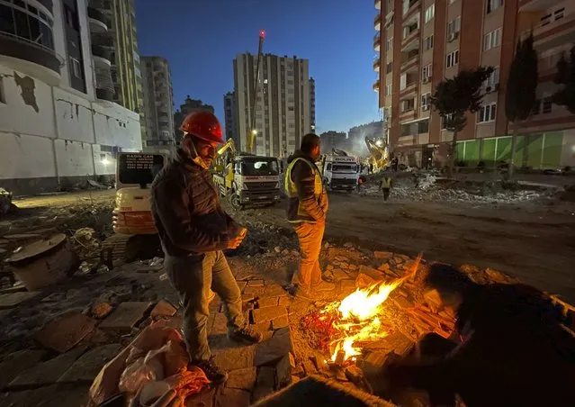 People try to stay warm around a fire as rescuers search in a destroyed building in Adana, southeastern Turkey, Thursday, February 9, 2023. Tens of thousands of people who lost their homes in a catastrophic earthquake huddled around campfires in the bitter cold and clamoured for food and water Thursday, three days after the temblor hit Turkey and Syria. (Photo by Lefteris Pitarakis/AP Photo)