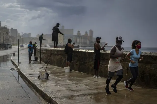 A couple wearing masks against the spread of the new coronavirus jog under the rain, past men fishing on the Malecon seawall, in Havana, Cuba, Tuesday, October 6, 2020. (Photo by Ramon Espinosa/AP Photo)