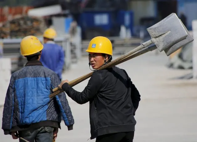 A woman worker, holding shovels, walks past a road construction site in Beijing, China, October 15, 2015. China's economic planner said it approved 218 fixed-asset projects worth 1.81 trillion yuan ($285.3 billion) in the first nine months of the year, as Beijing looks to drive infrastructure investment to support slowing economic growth. (Photo by Kim Kyung-Hoon/Reuters)