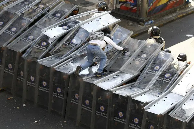 A demonstrator jumps on a shield wall formed by riot police during a protest against the government of Venezuela's President Nicolas Maduro, in Caracas, in this February 12, 2014 file photo. (Photo by Carlos Garcia Rawlins/Reuters)
