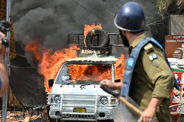A policeman stands near a burning vehicle during clashes between supporters of former prime minister Imran Khan and riot police near Khan's house to prevent officers from arresting him, in Lahore on early March 15, 2023. Pakistan police appeared on March 15 to have given up an attempt to arrest former prime minister Imran Khan, ending a siege of his residence after violent clashes with hundreds of his supporters. (Photo by Arif Ali/AFP Photo)