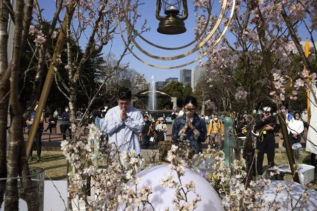 A man and a woman pray after laying flowers in front of a memorial set up to mark the 12th anniversary of the massive earthquake, tsunami and nuclear disaster, at Hibiya Park in Tokyo, Saturday, March 11, 2023. (Photo by Hiro Komae/AP Photo)