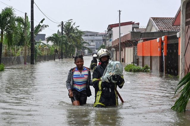 A firefighter guides a resident through flood water in Cocody Angre in Abidjan on June 14, 2024 after torrential rains. Flooding and landslips have killed five people in Abidjan, Ivory Coast's biggest city, after heavy downpours, the fire service said on Friday. Roads were cut off as the rains fell on Thursday afternoon in most areas of the city with a population of six million. (Photo by Issouf Sanogo/AFP Photo)