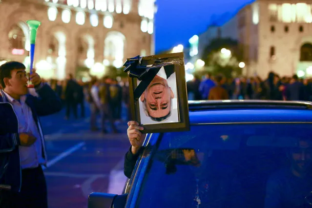 A protester holds a symbolic portrait of Prime Minister Serzh Sargsyan in a black frame as others gather to call for the resignation of Sargsyan, the former president who was appointed this week under a new government system that gives the prime minister expanded powers and diminishes the presidency, in Yerevan, Armenia, Friday, April 20, 2018. About 40,000 demonstrators gathered on the capital's central square as a week of large protests against the country's new leadership showed no sign of dissipating. (Photo by Hrant Khachatryan/PAN Photo via AP Photo)