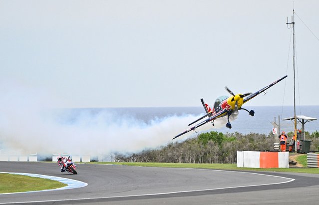 Former MotoGP World Champion Casey Stoner (L) powers through a corner as a plane flies during the Red Bull Air Display prior to the start of the MotoGP Australian Grand Prix on Philip Island on October 19, 2025. (Photo by Paul Crock/AFP Photo)