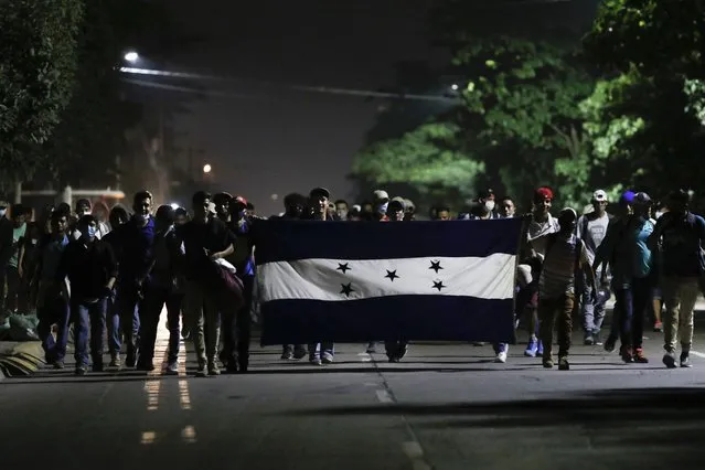Honduran migrants trying to reach the U.S. border walk along a highway carrying their national flag as they leave San Pedro Sula, Honduras, before dawn Friday, January 15, 2021. The group quickly dispersed along the heavily-trafficked highway to the border town of Agua Caliente, but estimates of their number ranged from 2,000 to more than twice that. (Photo by Delmer Martinez/AP Photo)