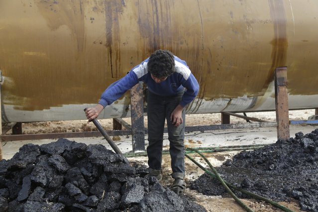 A youth works at a makeshift oil refinery site in Marchmarin town, southern countryside of Idlib, Syria December 16, 2015. The refinery site, owned by Yousef Ayoub, 34, has been active for 4 months. Ayoub says that he gets the crude oil from Islamic State-controlled areas in Deir al-Zor province and Iraq. The price for a barrel of crude oil varies and is controlled by the Islamic State, but it is currently at $44 dollars per barrel, he said. (Photo by Khalil Ashawi/Reuters)