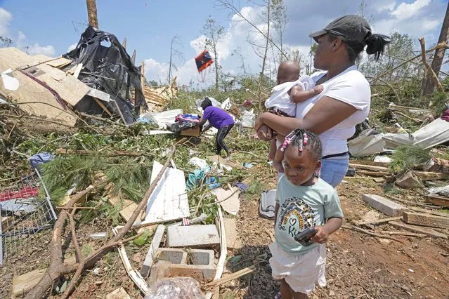 Dana Jackson holds her four month old daughter Brynlee Jackson, while she and daughter Genesis Jackson, three, watch relatives salvage personal items from a relative's mobile home that was demolished by an apparent Sunday night tornado that swept through Louin, Miss., Monday, June 19, 2023. Possible multiple tornadoes swept through Mississippi overnight, killing one and injuring nearly two dozen, officials said Monday. (Photo by Rogelio V. Solis/AP Photo)