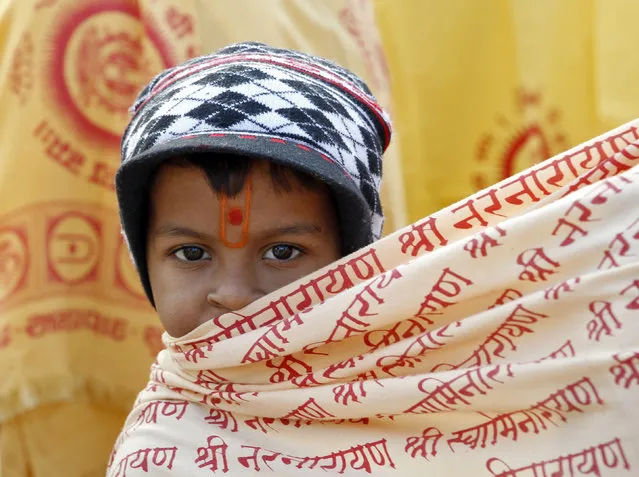 A Hindu boy wraps himself with a religious cloth to protect himself from cold as he waits for the start of the prayers on the first day of the five-day long mass prayer meetings for the world peace at a temple on the outskirts of Ahmedabad, India, December 23, 2015. (Photo by Amit Dave/Reuters)