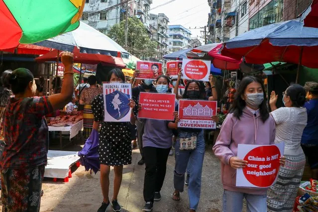 Anti-coup protesters hold slogans as they are greeted while marching along a market street in Yangon, Myanmar, Wednesday April 7, 2021. Threats of lethal violence and arrests of protesters have failed to suppress daily demonstrations across Myanmar demanding the military step down and reinstate the democratically elected government. (Photo by AP Photo/Stringer)