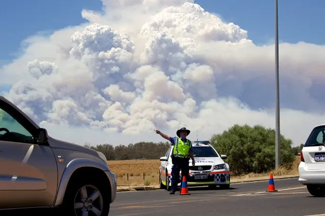 Smoke clouds from a large bush fire are seen behind a police road block at the turn off onto the South Western Highway near Pinjarra, Western Australia, January 7, 2016. (Photo by Richard Wainwright/Reuters/AAP)