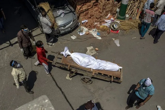 A man transports a dead body on a handcart to a ground that has been converted into a crematorium for mass cremation of COVID-19 victims, in New Delhi, India, Saturday, April 24, 2021. Delhi has been cremating so many bodies of coronavirus victims that authorities are getting requests to start cutting down trees in city parks, as a second record surge has brought India's tattered healthcare system to its knees. (Photo by Altaf Qadri/AP Photo)