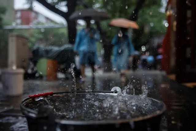 A bucket overflows with rain water during a downpour in Beijing, China on July 30, 2023. (Photo by Thomas Peter/Reuters)