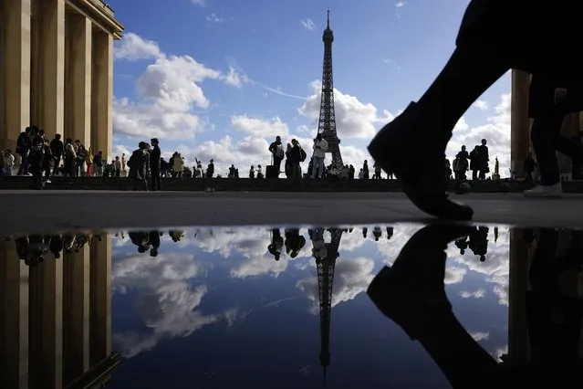 The Eiffel Tower is reflected in a puddle as people walk past at the Trocadero square, in Paris, France, Tuesday, October 24, 2023. (Photo by Pavel Golovkin/AP Photo)