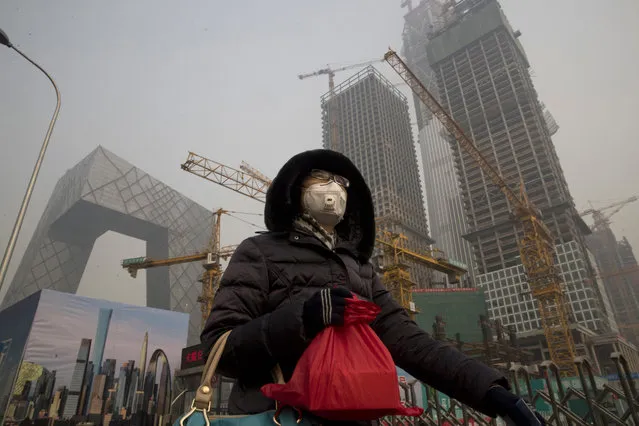 A woman wears a mask as she walks past a construction site as smog continues to choke Beijing on Friday, January 6, 2017. The official Xinhua News Agency reported this week that the environmental ministry had given out punishments after finding that more than 500 construction sites and enterprises, including metallurgy, agricultural chemical and steel plants, and 10,000 vehicles had breached pollution response plans. (Photo by Ng Han Guan/AP Photo)