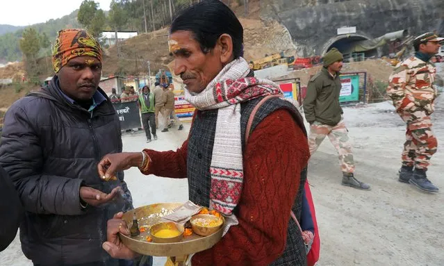 A local Hindu priest (C) distributes offerings to a worker arriving at the site of the Silkyara tunnel that collapsed while being under construction, to join in rescue operations, in Uttarkashi, India on November 27, 2023. Rescue and relief operations continue for the 41 workers who remain trapped after the tunnel on the Brahmakal Yamunotri National Highway collapsed on 12 November 2023. The workers were expected to be rescued on 24 November but operations were halted due to some technical glitch. The Indian Army has also joined the rescue operations and a vertical drilling was started as another option. A team of miners was assigned to start manual drilling and digging by hand to reach the trapped workers. (Photo by Harish Tyagi/EPA/EFE)