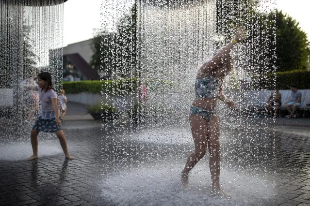 Children cool off in a public fountain in Vilnius, Lithuania, Thursday, July 15, 2021. The heat wave continues in Lithuania as temperature rise to as high as 32 degrees Celsius (89.6 degrees Fahrenheit). (Photo by Mindaugas Kulbis/AP Photo)