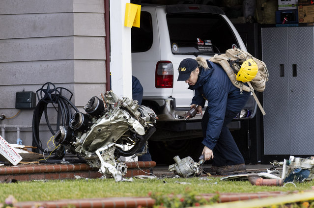 A National Transportation Safety Board worker takes a photo of an engine that came to rest against a house on Crestknoll Dr. in Yorba Linda, Calif on Monday, February 4, 2019. The debris field from a small plane crash a day earlier covered several blocks with one home catching fire. The pilot and four people on the ground died. (Photo by Paul Bersebach/The Orange County Register via AP Photo)