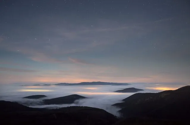A photo made available on 28 December 2015 at Dobogoko hikers' lookout spot shows peaks of the Visegradi Mountain rising above a blanket of fog, which is illuminated from beneath by the lights emanating from settlements near Pilisszentkereszt, 30 kms northwest of Budapest, Hungary, 27 December 2015. (Photo by Balazs Mohai/EPA)
