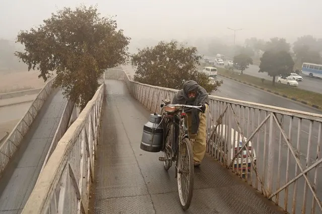 A milkman pushes his bicycle through a pedestrian bridge on a cold foggy winter morning in Islamabad on January 3, 2024. (Photo by Aamir Qureshi/AFP Photo)
