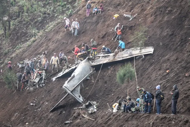 People inspect the wreckage of an Indonesia's Air Force EMB-314 Super Tucano plane that crashed in Pasuruan, East Java, on November 17, 2023. Four people, including two pilots, were killed in Indonesia on November 16 when two military aircraft crashed into a mountainside during training, an air force spokesperson said. Two Embraer Super Tucano planes took off from the East Java city of Malang on Thursday morning before losing contact half an hour later during regular formation training. (Photo by Ahmad Mahdi/AFP Photo)