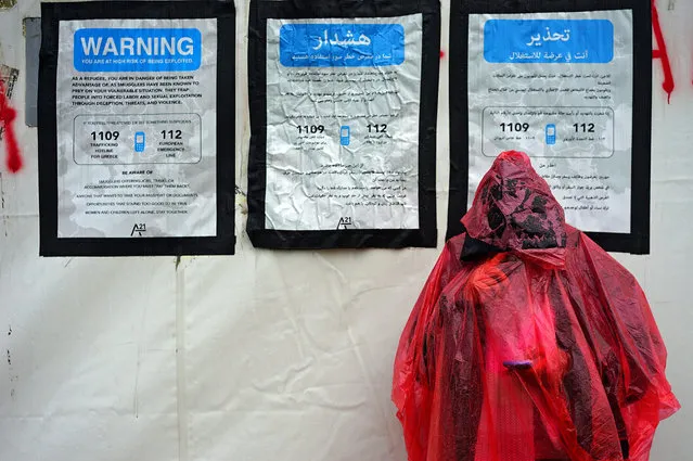 A refugee reads his mobile phone under plastic cover in front of advises to refugees during rain in a refugees camp at the border between Greece and the Former Yugoslav Republic of Macedonia (FYROM), near Idomeni, Greece, 12 March 2016. After Slovenia, Croatia, Serbia and Macedonia have sealed their borders to the migration flow, tens of thousands of people are left stranded in Greece, where most migrants enter the European Union to continue on to countries in western and northern Europe. (Photo by Nake Batev/EPA)