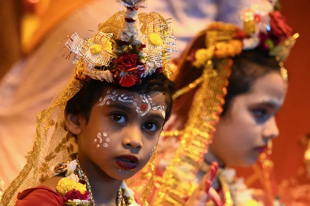 A girl looks on next to others dressed as Hindu Goddess Durga at a temporary worship place during the Durga Puja festival in Kolkata on October 13, 2021. (Photo by Dibyangshu Sarkar/AFP Photo)