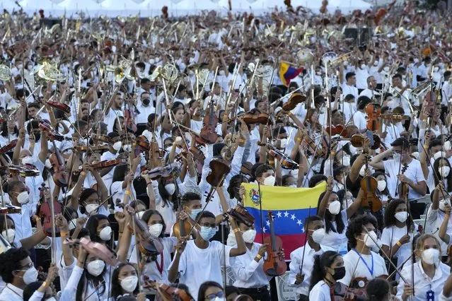 Members of the National Orchestra System raise their instruments after they played a 12-minute Piotr's Slavic March Ilich Tchaikovsky to try and break a Guinness World Record, in Caracas, Venezuela, Saturday, November 13, 2021. (Photo by Ariana Cubillos/AP Photo)