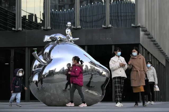 Residents wearing masks past by an art work outside a mall in Beijing, China, on November 13, 2021. Quarantines, obligatory testing and travel restrictions have become a way of life for much of the population. The country's vaccination rate is among the world's highest and authorities are beginning to administer booster shots as winter descends. (Photo by Ng Han Guan/AP Photo)