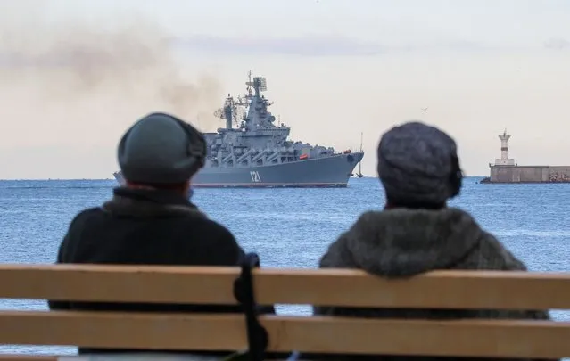 Women sit on a bench as the Russian Navy's guided missile cruiser Moskva (Moscow) sails back into a harbour after tracking NATO warships in the Black Sea, in the port of Sevastopol, Crimea on November 16, 2021. (Photo by Alexey Pavlishak/Reuters)