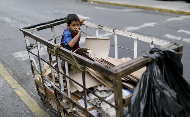 A boy sits in a recycler's cart in Caracas, Venezuela, Saturday, May 4, 2019. (Photo by Ariana Cubillos/AP Photo)
